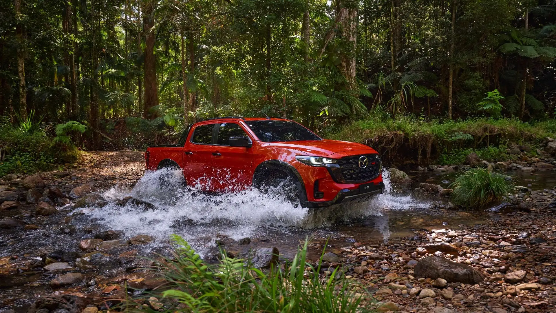 Red Mazda BT-50 pickup crossing a river at speed